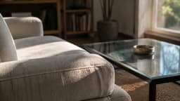 Sunlit cotton sofa and glass coffee table in a clear-air living room, illustrating surfaces where smoke residue may settle.
